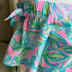 Puede incluir: Top con hombros descubiertos con un vibrante estampado floral en rosa, turquesa y verde. La tela est&aacute; fruncida en el escote y las mangas, con peque&ntilde;os lazos en los hombros. La parte superior est&aacute; hecha de una tela ligera estampada.