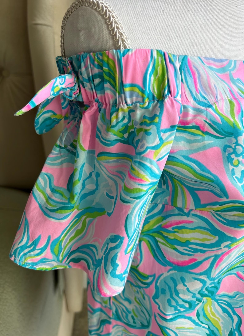 Puede incluir: Top con hombros descubiertos con un vibrante estampado floral en rosa, turquesa y verde. La tela est&aacute; fruncida en el escote y las mangas, con peque&ntilde;os lazos en los hombros. La parte superior est&aacute; hecha de una tela ligera estampada.