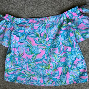 Puede incluir: Top rosa con hombros descubiertos y estampado floral turquesa y verde. El top tiene mangas cortas y lazos en los hombros. La tela est&aacute; estampada con flores estilizadas, ofreciendo un estilo veraniego y femenino. Fabricado con tejido ligero.