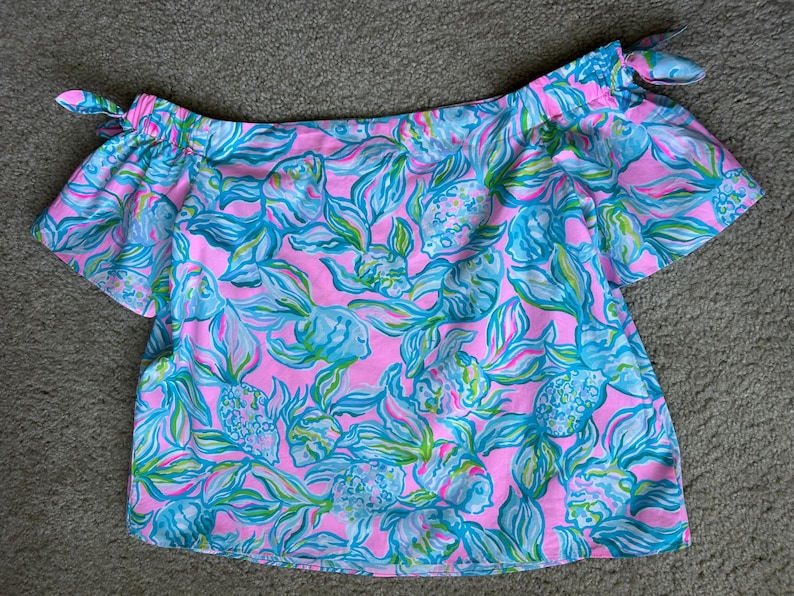 Puede incluir: Top rosa con hombros descubiertos y estampado floral turquesa y verde. El top tiene mangas cortas y lazos en los hombros. La tela est&aacute; estampada con flores estilizadas, ofreciendo un estilo veraniego y femenino. Fabricado con tejido ligero.