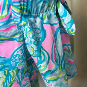 Puede incluir: Top con hombros descubiertos con un estampado vibrante y colorido. La tela presenta un patr&oacute;n de remolinos y formas rosas, azules, verdes y blancos. Las mangas est&aacute;n recogidas y atadas con lazos. Una prenda brillante y alegre.