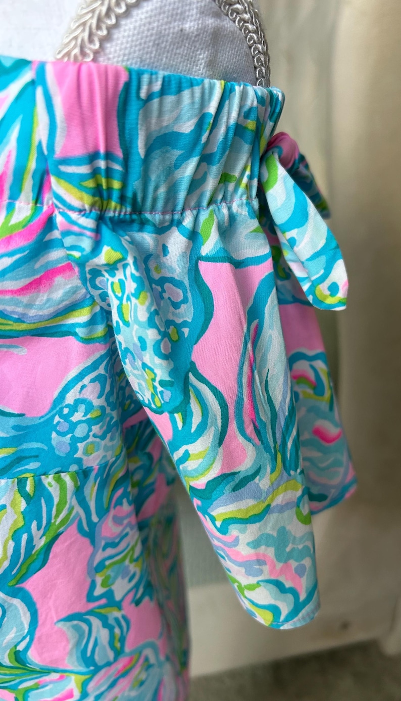 Puede incluir: Top con hombros descubiertos con un estampado vibrante y colorido. La tela presenta un patr&oacute;n de remolinos y formas rosas, azules, verdes y blancos. Las mangas est&aacute;n recogidas y atadas con lazos. Una prenda brillante y alegre.