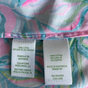 Puede incluir: Primer plano de una tela con un colorido estampado floral en tonos rosa, azul y verde. La tela tiene dos etiquetas blancas con texto, incluyendo "100% Algod&oacute;n Exclusivo de Decoraci&oacute;n" y "Hecho en Indonesia".