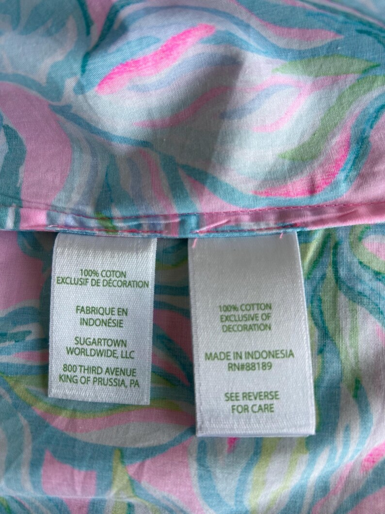 Puede incluir: Primer plano de una tela con un colorido estampado floral en tonos rosa, azul y verde. La tela tiene dos etiquetas blancas con texto, incluyendo "100% Algod&oacute;n Exclusivo de Decoraci&oacute;n" y "Hecho en Indonesia".