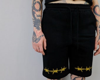 May include: Black sweatpants with a drawstring waist and gold barbed wire detail at the bottom of the legs.