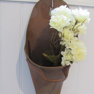May include: A brown metal wall planter shaped like a shoe with a white flower arrangement inside.