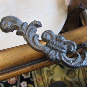 Puede incluir: Primer plano de un acento decorativo de metal negro con un diseño de desplazamiento. El acento está unido a una silla de madera.