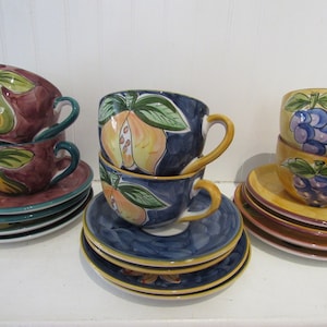 May include: Set of three ceramic teacups and saucers with fruit designs. The cups are stacked and feature pears, quince, and grapes. The saucers are in coordinating colors and patterns.