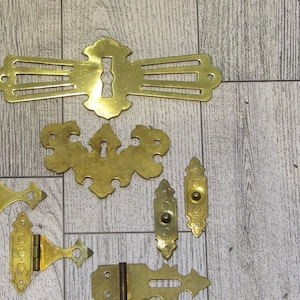 以下が含まれることがあります： ヒンジ、キーホールカバー、装飾的なアクセントなど、8つのアンティーク真鍮製の金具のセット。これらの金具は、複雑なデザインと、使い込まれたようなアンティークな仕上げが特徴です。