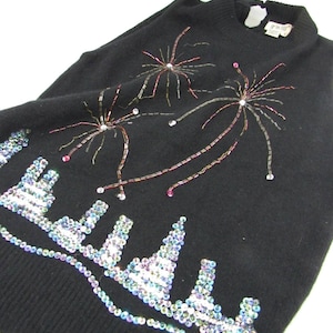 May include: Black sleeveless sweater with a sequined design of fireworks and a city skyline. The sweater is made of a soft, knit fabric.