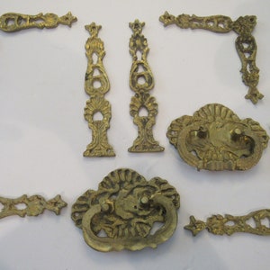 May include: Set of eight antique brass drawer pulls and corner pieces. The pulls have a decorative, ornate design with a scalloped edge. The corner pieces are also ornate and have a scalloped edge.