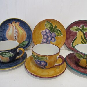 May include: Set of six ceramic teacups and saucers with fruit designs. The cups and saucers feature a variety of fruits, including pears, grapes, and pomegranates. The designs are painted in bright colors on a white background.