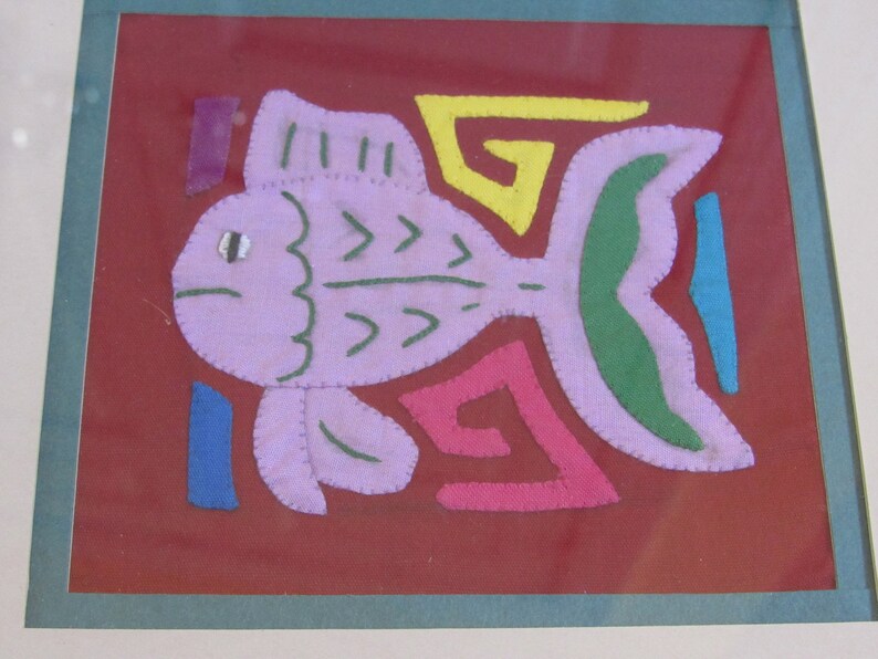May include: A framed artwork featuring a purple fish with green and yellow details, surrounded by colorful geometric shapes on a red background.