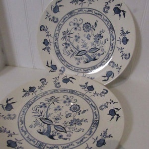 May include: Two white ceramic dinner plates with a blue floral pattern. The pattern features a central floral motif with smaller floral designs around the edge.