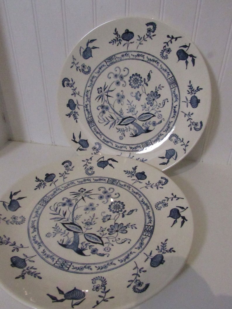 May include: Two white ceramic dinner plates with a blue floral pattern. The pattern features a central floral motif with smaller floral designs around the edge.