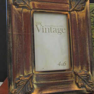 K&ouml;nnte beinhalten: Ein verwitterter Holzbilderrahmen mit einer Blattgold-Oberfl&auml;che. Der Rahmen hat an jeder Ecke ein erhabenes Blattdesign und tr&auml;gt die Aufschrift "Philip Whitney Ltd. Vintage" und "4x6" auf der Vorderseite.