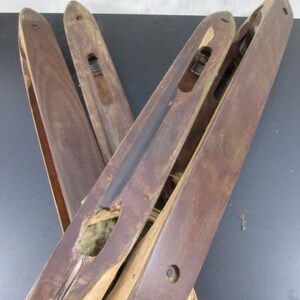 May include: Four wooden weaving shuttles with a dark brown finish. The shuttles have a groove down the centre and a small hole at one end. The shuttles are in a criss-cross pattern.