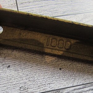 May include: A brass metal bracket with two holes and the number "1000" stamped on the surface.