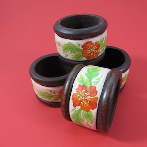 May include: Four wooden napkin rings with a white background and orange flower designs. The rings are stacked on top of each other.