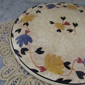 May include: Oval ceramic serving platter with a cream-colored background and a floral design. The flowers are yellow, blue, and red, with black stems and leaves. The edge of the platter is black.