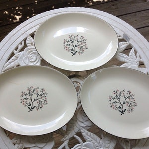Puede incluir: Tres platos de servir ovalados blancos con borde dorado y un diseño floral en rosa y verde.