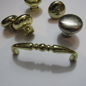 May include: A collection of gold-toned cabinet hardware, including several mushroom-shaped knobs and a decorative pull handle. The hardware is made of metal and has a shiny finish, suitable for furniture restoration or new builds.