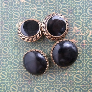 May include: Four round buttons with black centres and gold decorative trim. The buttons are on a green and gold patterned surface.