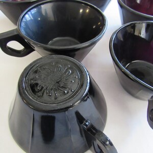 May include: Set of black and purple glass teacups with a decorative design on the bottom. The cups have a glossy finish and are perfect for serving tea or coffee.