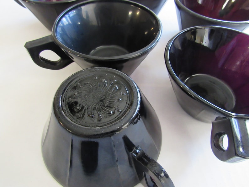 May include: Set of black and purple glass teacups with a decorative design on the bottom. The cups have a glossy finish and are perfect for serving tea or coffee.
