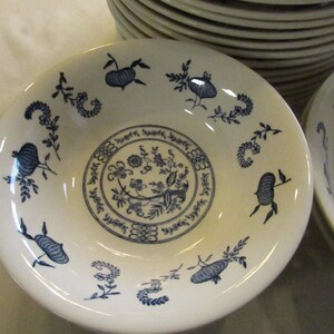 May include: A white ceramic bowl with a blue floral design. The bowl has a wide rim and a deep well. The floral design is intricate and features a variety of flowers and leaves.