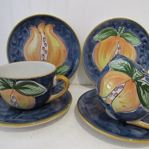 May include: Set of four ceramic teacups and saucers with a blue background and a hand-painted design of pomegranates in shades of orange, yellow, and green.