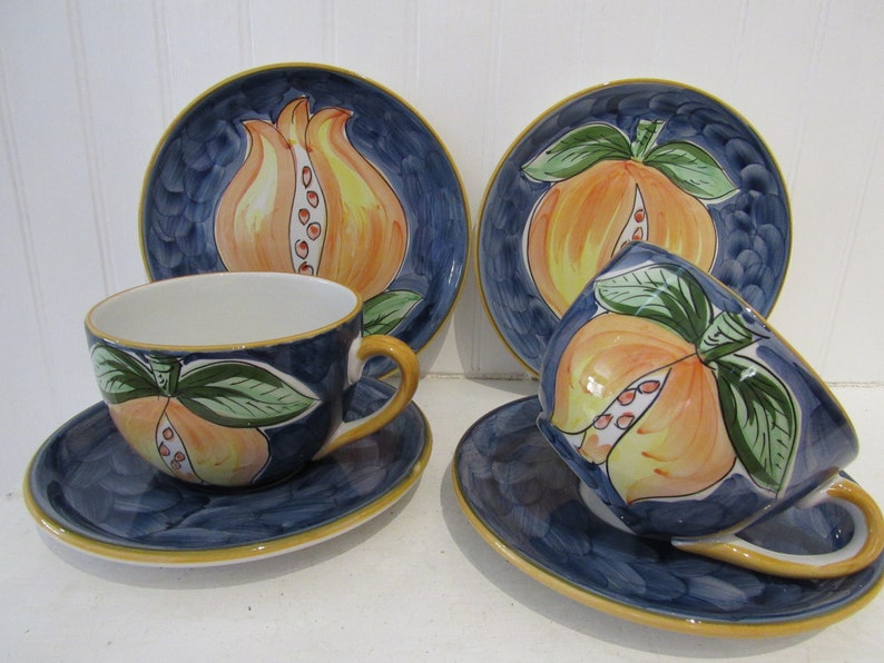 May include: Set of four ceramic teacups and saucers with a blue background and a hand-painted design of pomegranates in shades of orange, yellow, and green.