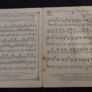 May include: A vintage sheet music book with two songs: "Don't Let That Moon Get Away" and "I've Got A Pocketful Of Dreams". The sheet music is printed on yellowed paper with black ink. The book is open to the second song, "I've Got A Pocketful Of Dreams".