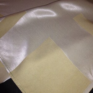 Peut inclure: Une nappe blanche avec des rayures beiges. La nappe est en tissu soyeux et a un léger brillant.