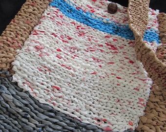 May include: A handmade tote bag crafted from recycled plastic strips in shades of white, gray, tan, and blue. The bag features a thick woven strap, a textured knit-like pattern, and a single dark brown circular button closure at the top center.