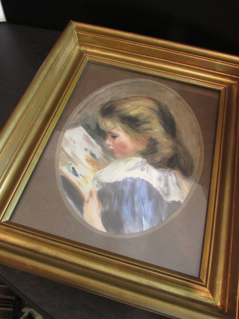 May include: A framed painting of a young girl in a blue dress reading a book. The painting is set in an oval frame and has a brown background.