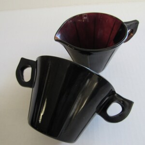 May include: A set of two vintage glass creamer and sugar bowls. The creamer is a deep purple color and the sugar bowl is black.