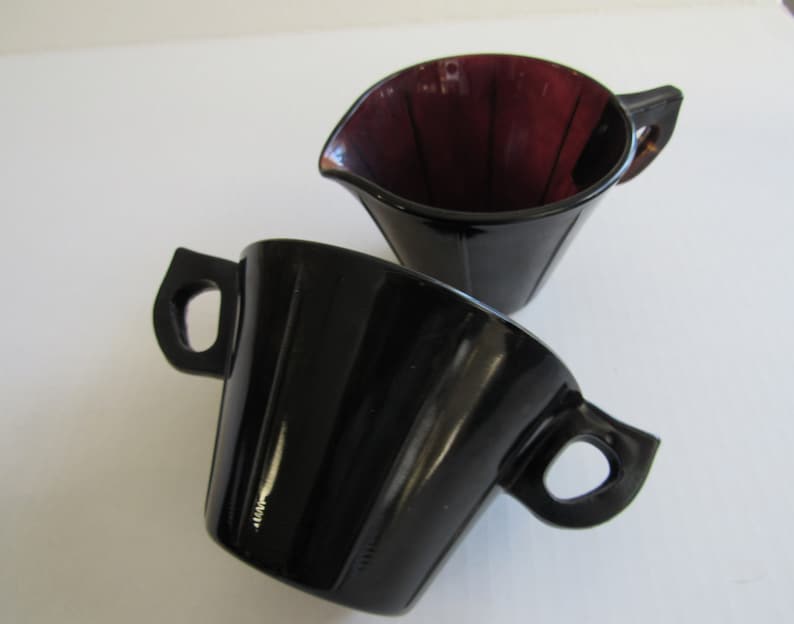 May include: A set of two vintage glass creamer and sugar bowls. The creamer is a deep purple color and the sugar bowl is black.