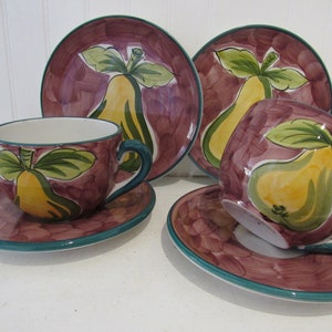 May include: Set of four ceramic teacups and saucers with a pear design. The cups and saucers are decorated with a purple background and green leaves. The pears are yellow with green leaves.