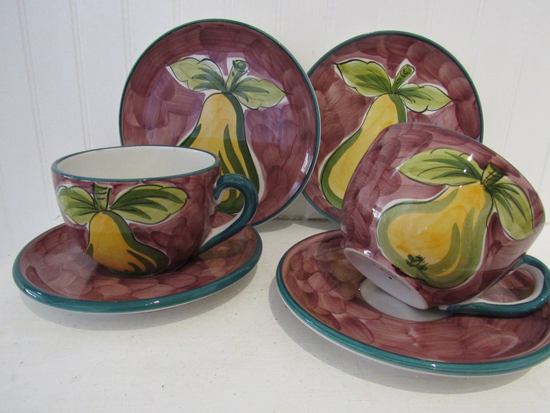 May include: Set of four ceramic teacups and saucers with a pear design. The cups and saucers are decorated with a purple background and green leaves. The pears are yellow with green leaves.