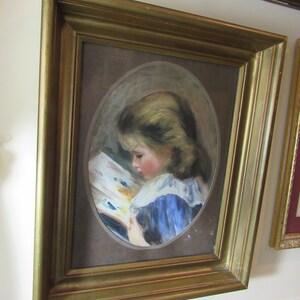 May include: A framed painting of a young girl in a blue dress reading a book. The painting is set against a brown background and is framed in a gold frame.