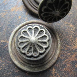 May include: Close-up of a silver metal knob with a decorative floral design. The knob is mounted on a dark brown surface.