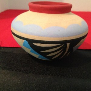 May include: A small, hand-painted ceramic pot with a red rim, blue, black, and white geometric designs.