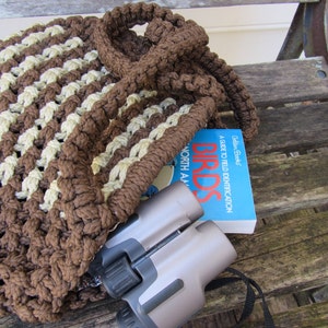 May include: A brown and beige crocheted tote bag with a book titled "Birds: A Guide to Field Identification" by Golden Books and a pair of binoculars inside.