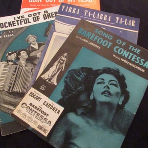 May include: A stack of four vintage sheet music books with blue, red, and black covers. The top book is titled "Goin' Out of My Head" and the bottom book is titled "Song of the Barefoot Contessa".
