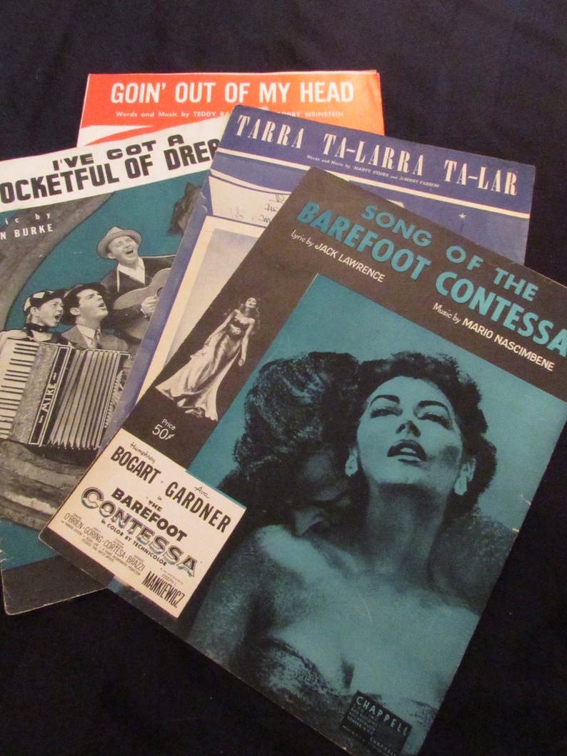 May include: A stack of four vintage sheet music books with blue, red, and black covers. The top book is titled "Goin' Out of My Head" and the bottom book is titled "Song of the Barefoot Contessa".