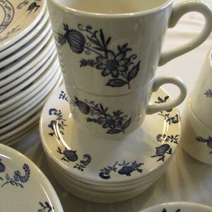 May include: A set of white ceramic teacups and saucers with a blue floral pattern. The cups have a rounded shape and a handle on the side. The saucers have a scalloped edge.