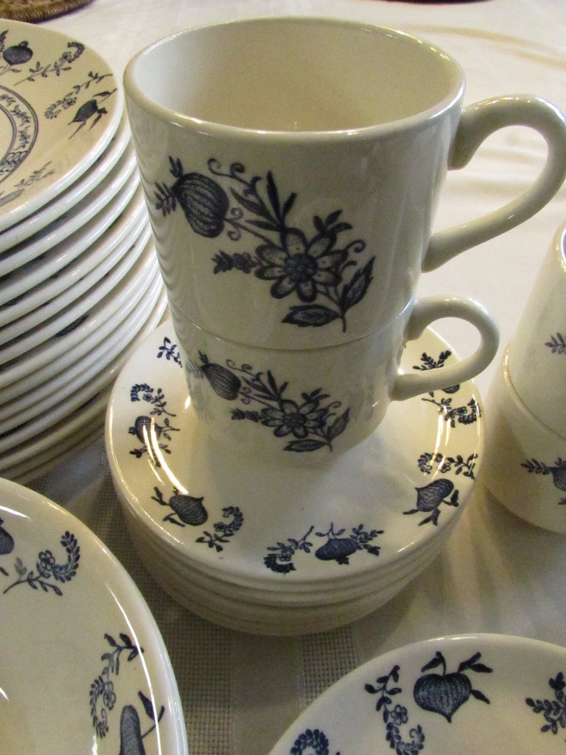 May include: A set of white ceramic teacups and saucers with a blue floral pattern. The cups have a rounded shape and a handle on the side. The saucers have a scalloped edge.