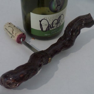 May include: A wooden bottle opener with a dark brown finish and a metal corkscrew. The opener is shaped like a twisted branch.