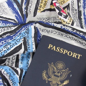 May include: A blue passport with the word "PASSPORT" printed in gold letters. The passport is lying on top of a white and blue patterned fabric with black writing.